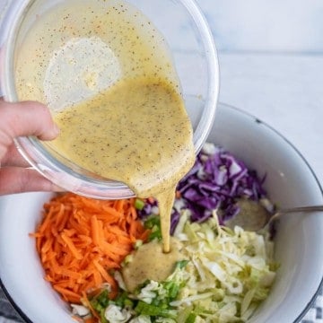 coleslaw ingredients in wedge sections in a white bowl with a POV of a hand pouring in the coleslaw dressing on the top