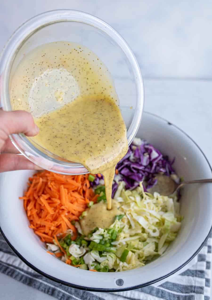 coleslaw ingredients in wedge sections in a white bowl with a POV of a hand pouring in the coleslaw dressing on the top