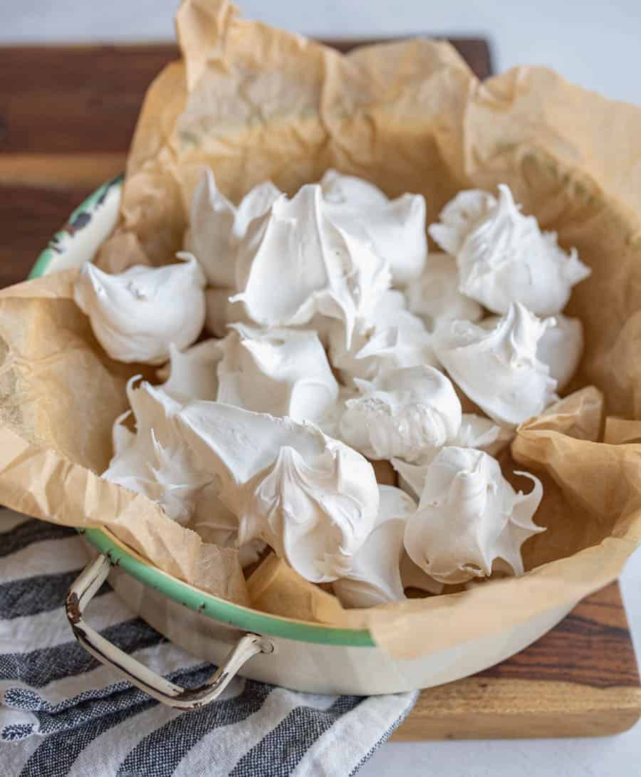 dollops of fluffy looking white divinity candy on parchment stacked in a dish.