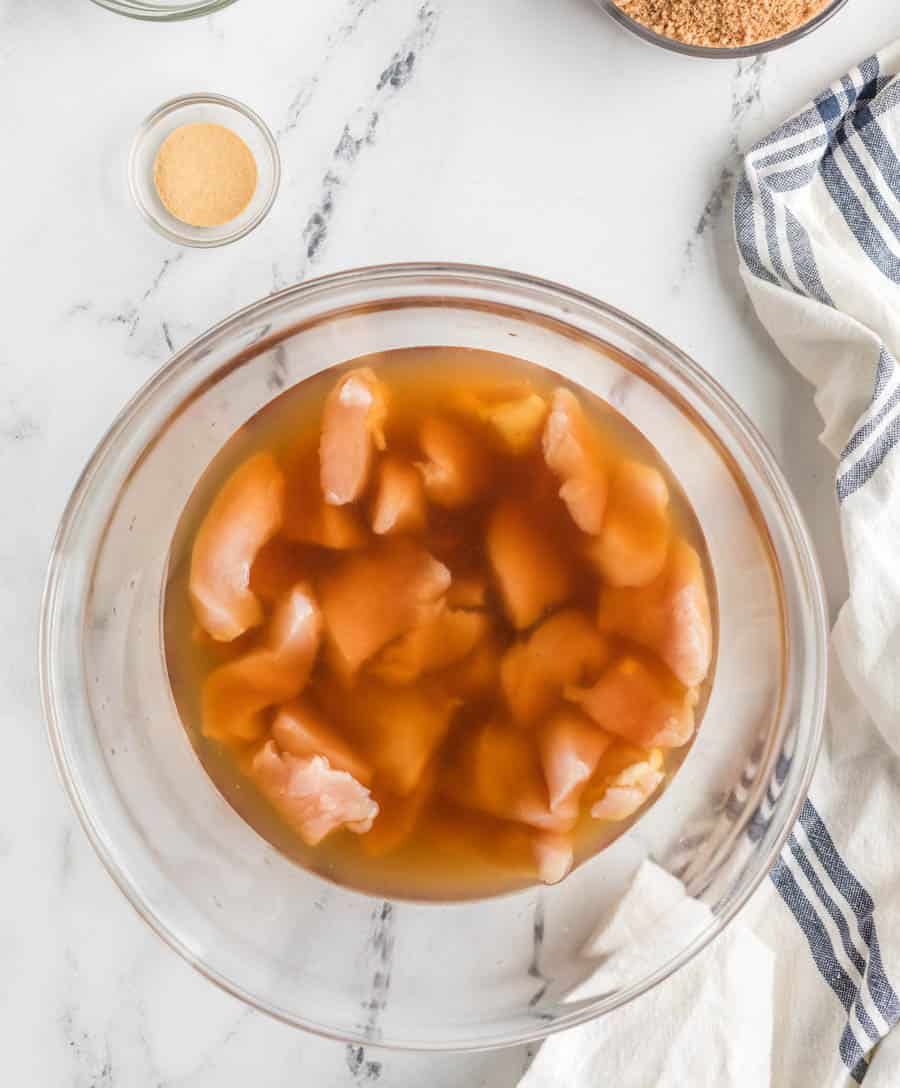 raw chicken soaking in a marinade in a clear glass bowl.