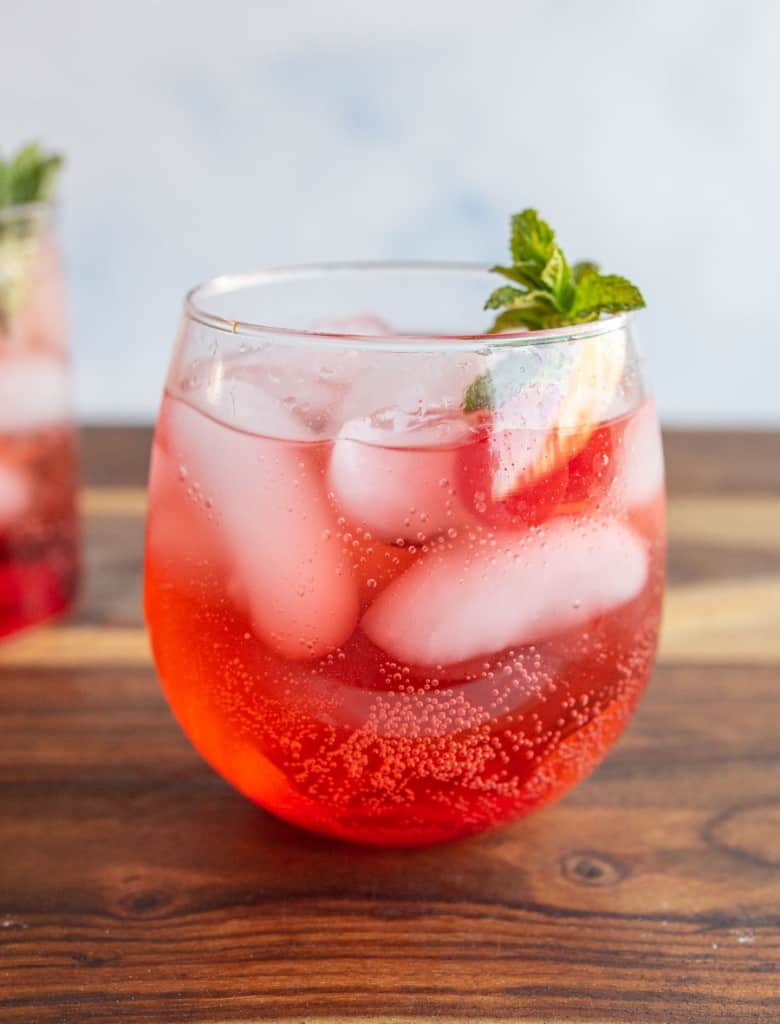 round tumbler of a red "Shirley-Temple" drink with ice cherries and garnish