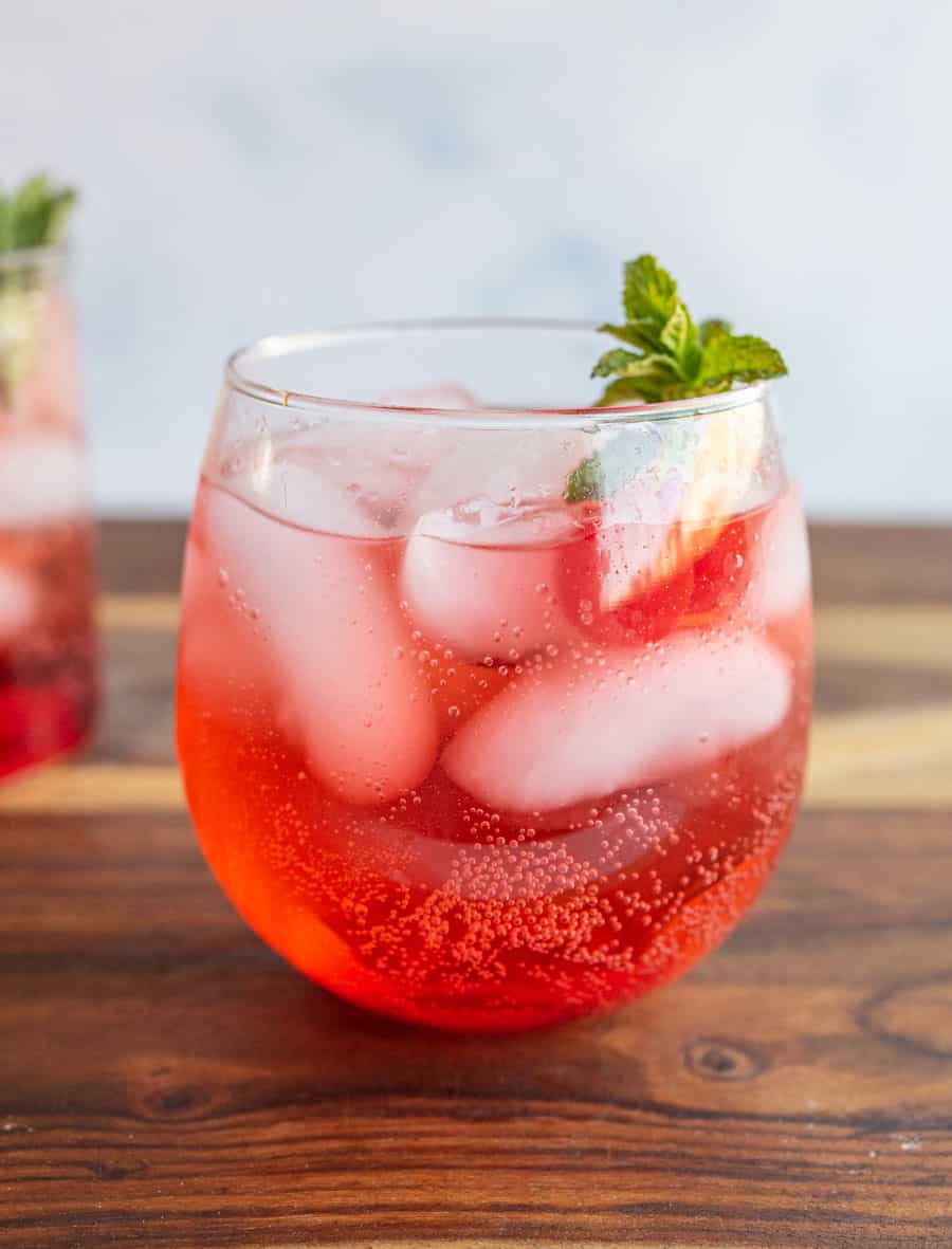 round tumbler of a red "Shirley-Temple" drink with ice cherries and garnish