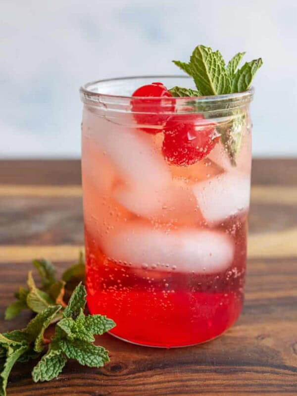 tumbler of a red "Shirley-Temple" drink with ice cherries and garnish