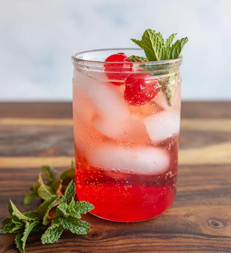 tumbler of a red "Shirley-Temple" drink with ice cherries and garnish