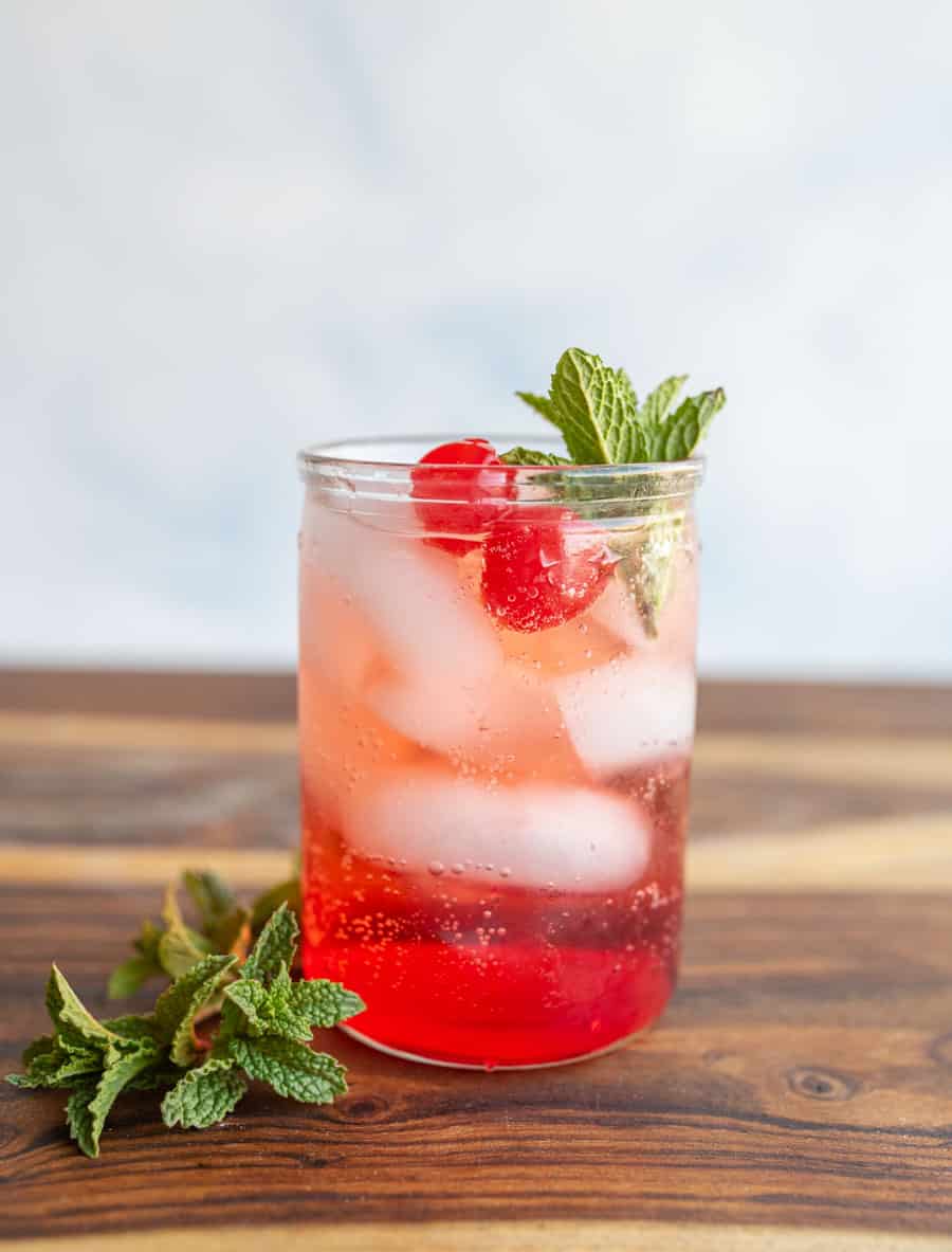 tumbler of a red "Shirley-Temple" drink with ice cherries and garnish