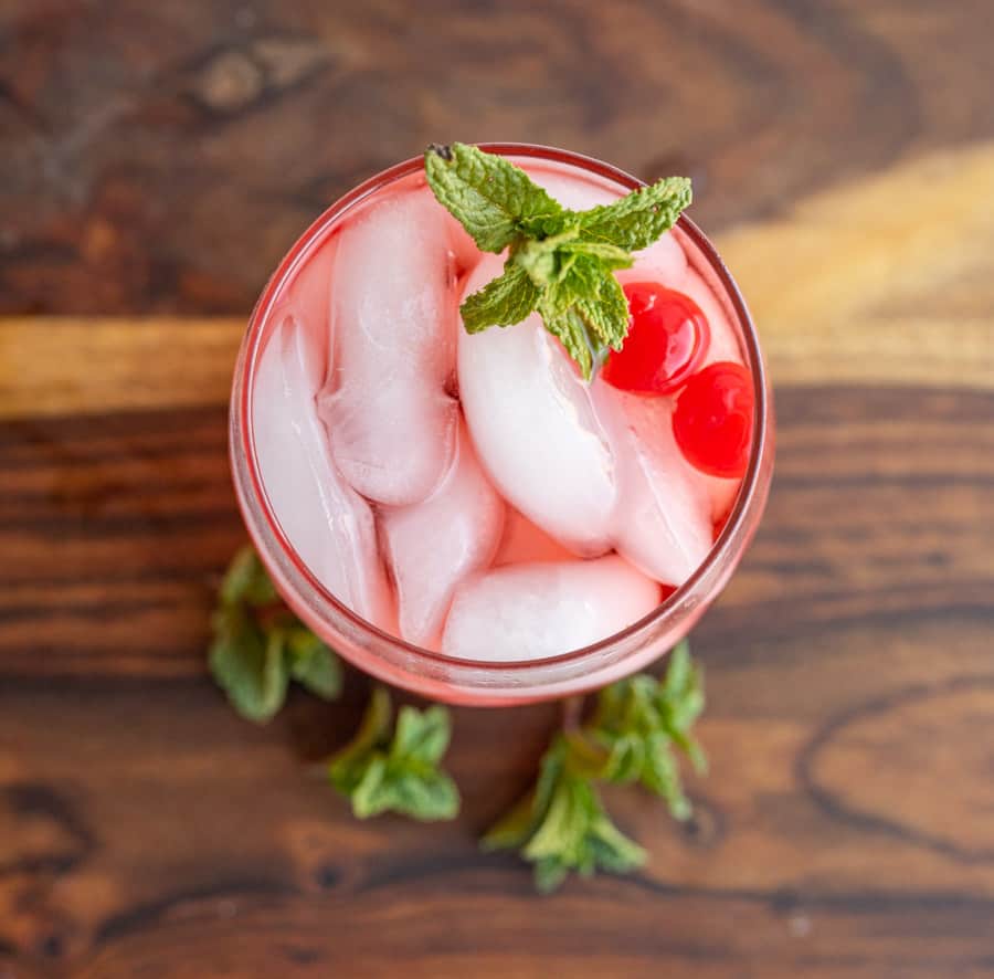 top view tumbler of a red "Shirley-Temple" drink with ice cherries and garnish
