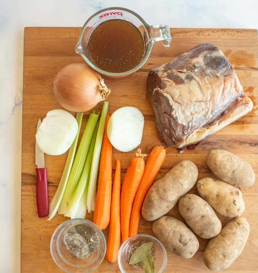 ingredients for beef stew on a cutting board potato carrots celery onion and beef.