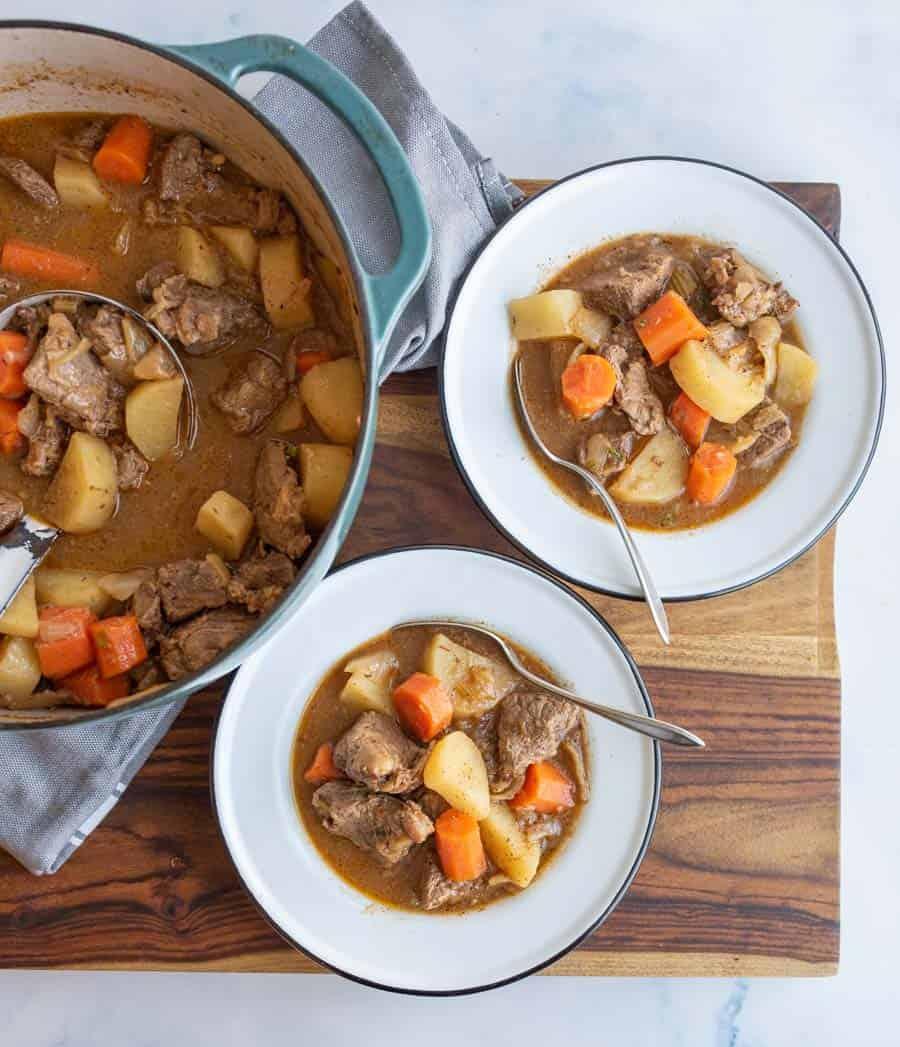 dutch oven with beef stew and two bowls served to the side