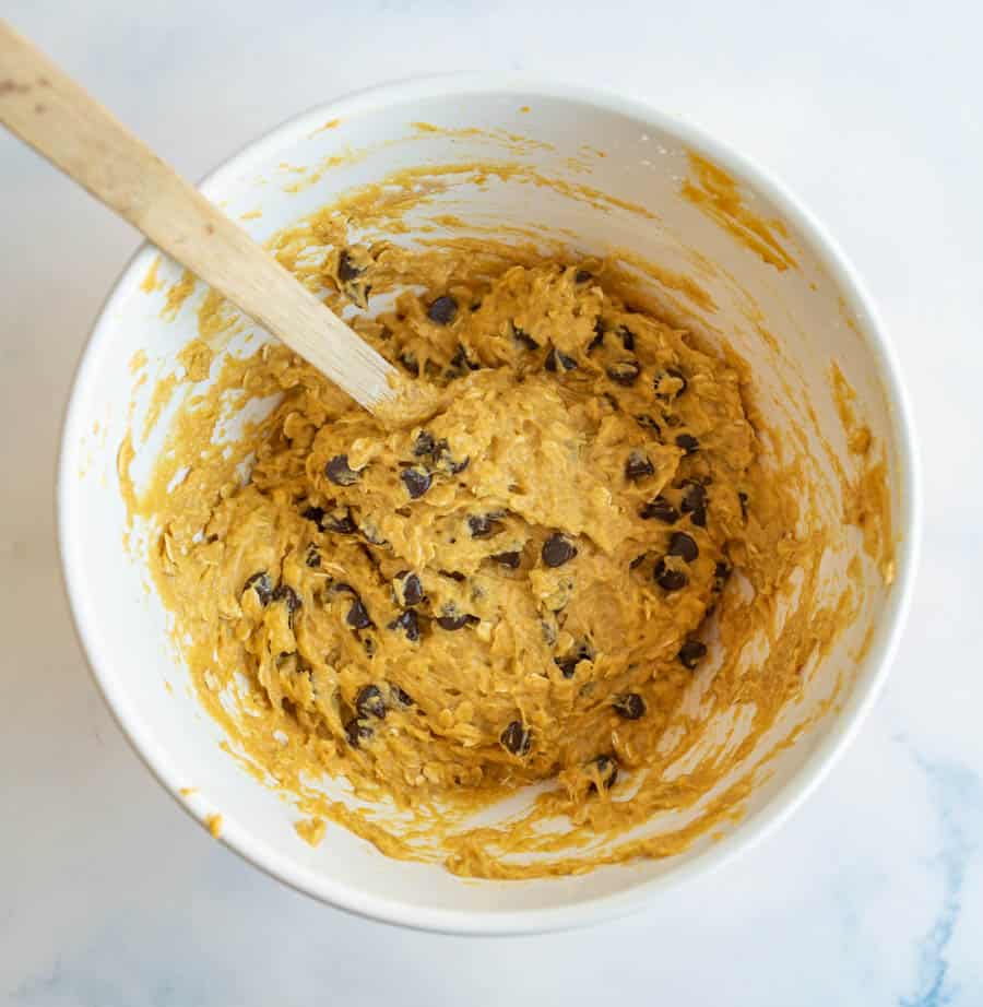 breakfast cookie batter in a white mixing bowl and a spoon stirring them