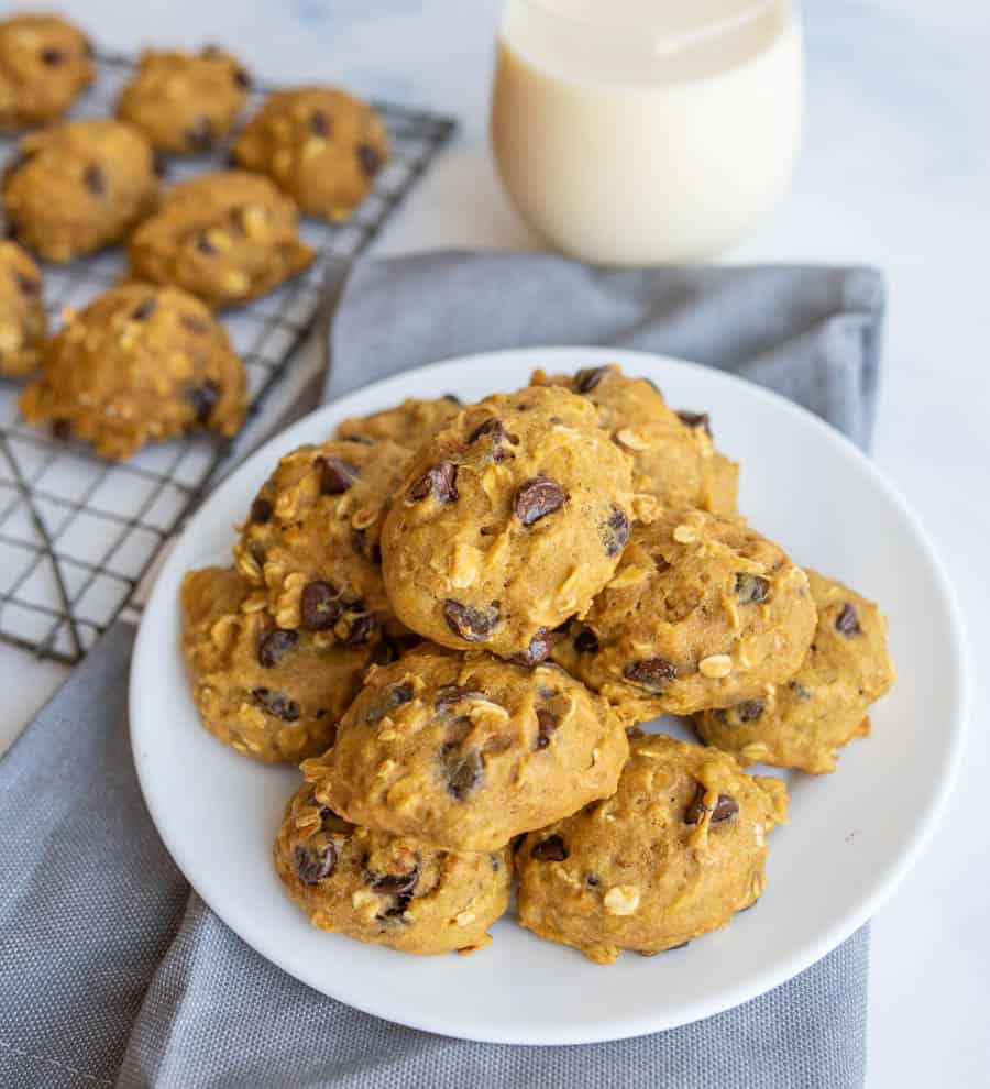 stacked breakfast cookies on a white plate with some on a cooling rack and a glass of milk in the background