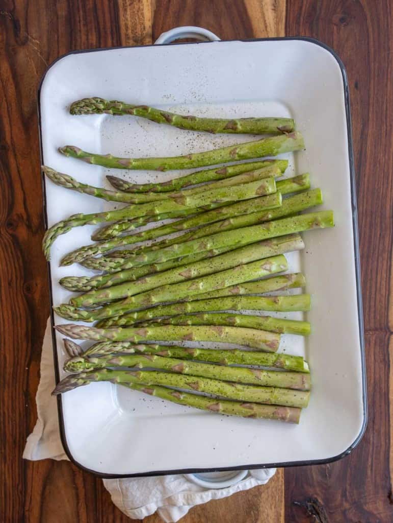 salt and pepper on raw asparagus on a white baking tray