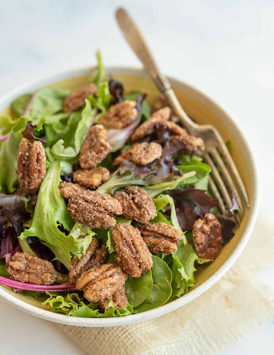 candied pecans on top mixed spring greens in a salad bowl