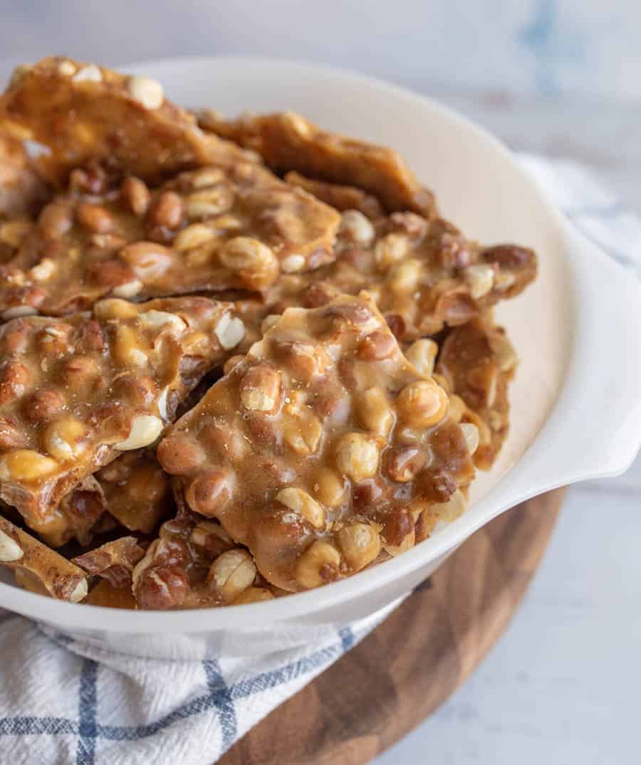 a close up of a white bowl with shards of homemade peanut brittle