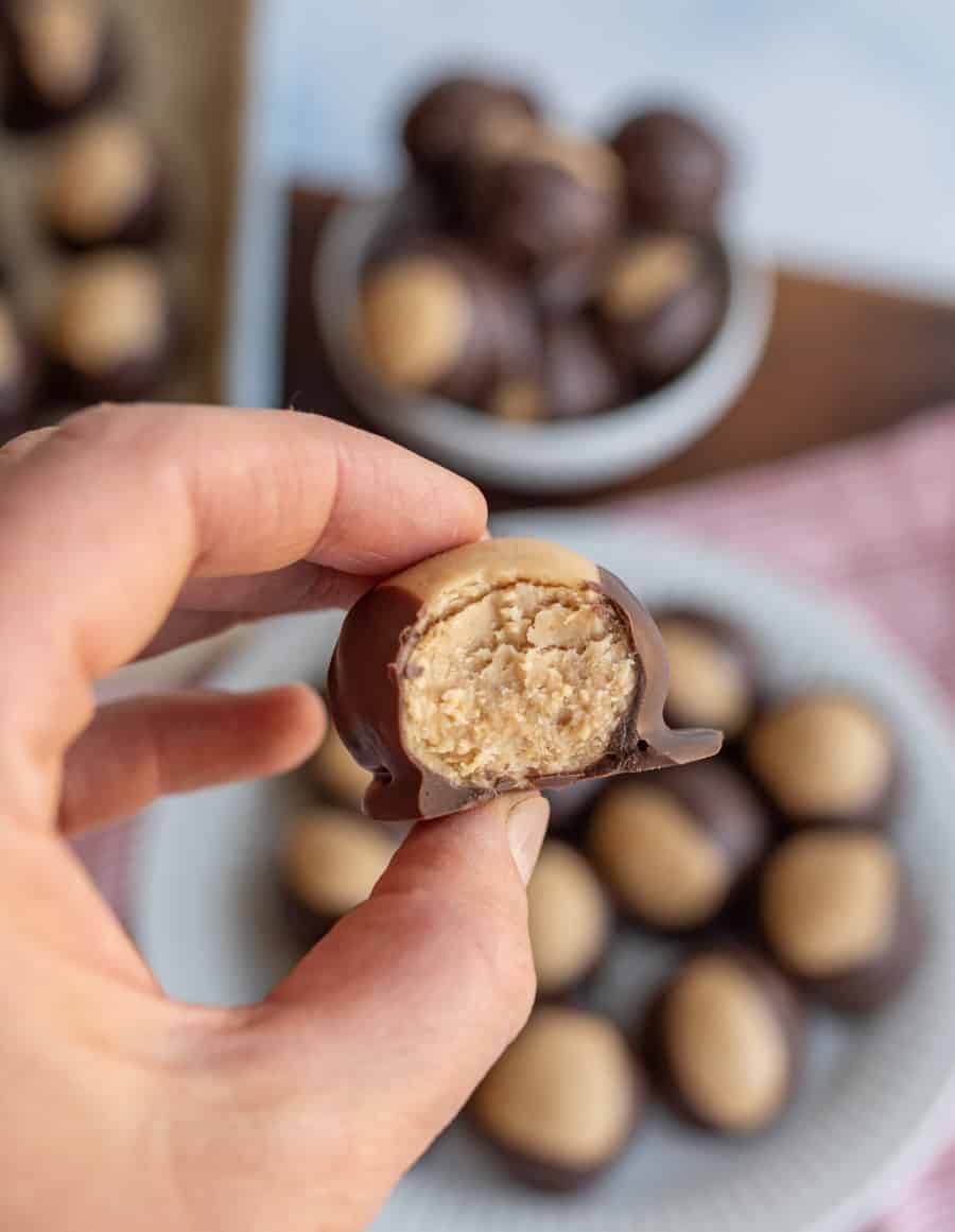 peanut butter chocolate buckeye bites with a hand holding a buckeye with a bite out of the chocolate exterior and filled center.