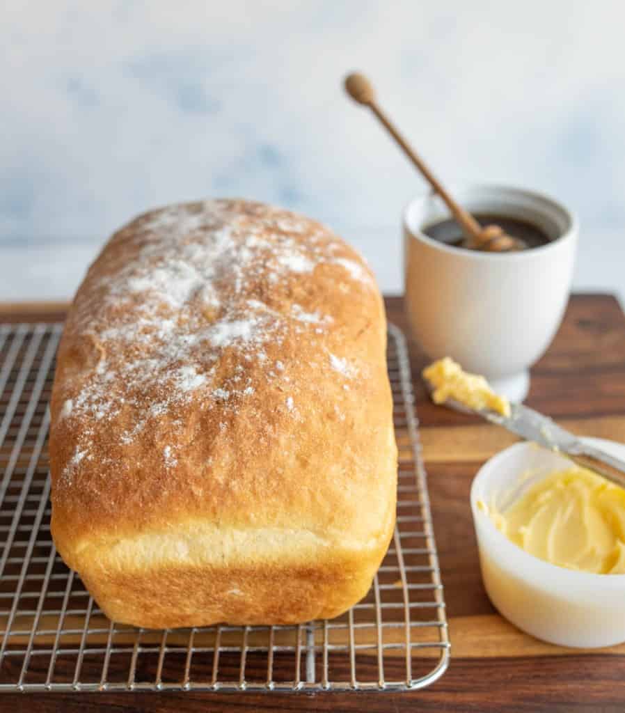 whole loaf of baked potato bread on cooling rack with flour on top and honey and butter on the side