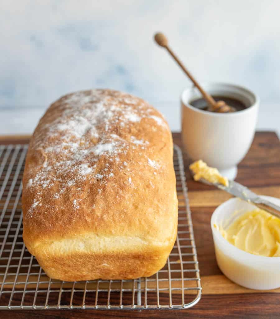 whole loaf of baked potato bread on cooling rack with flour on top and honey and butter on the side.