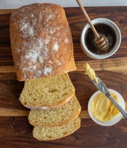 top view of a loaf of sliced airy potato bread with honey and butter in the background