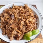 photo of shredded pork on a white plate with fresh lime