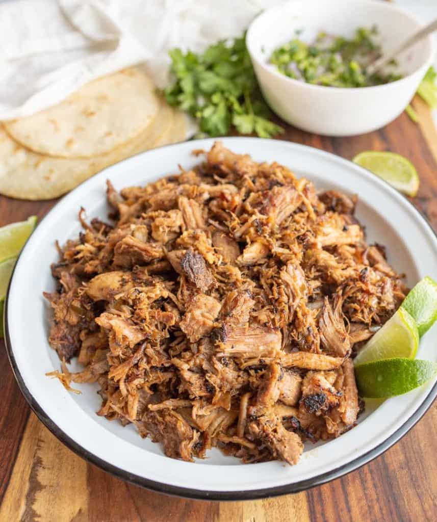 shredded pork on a white plate with carnitas ingredients in the background