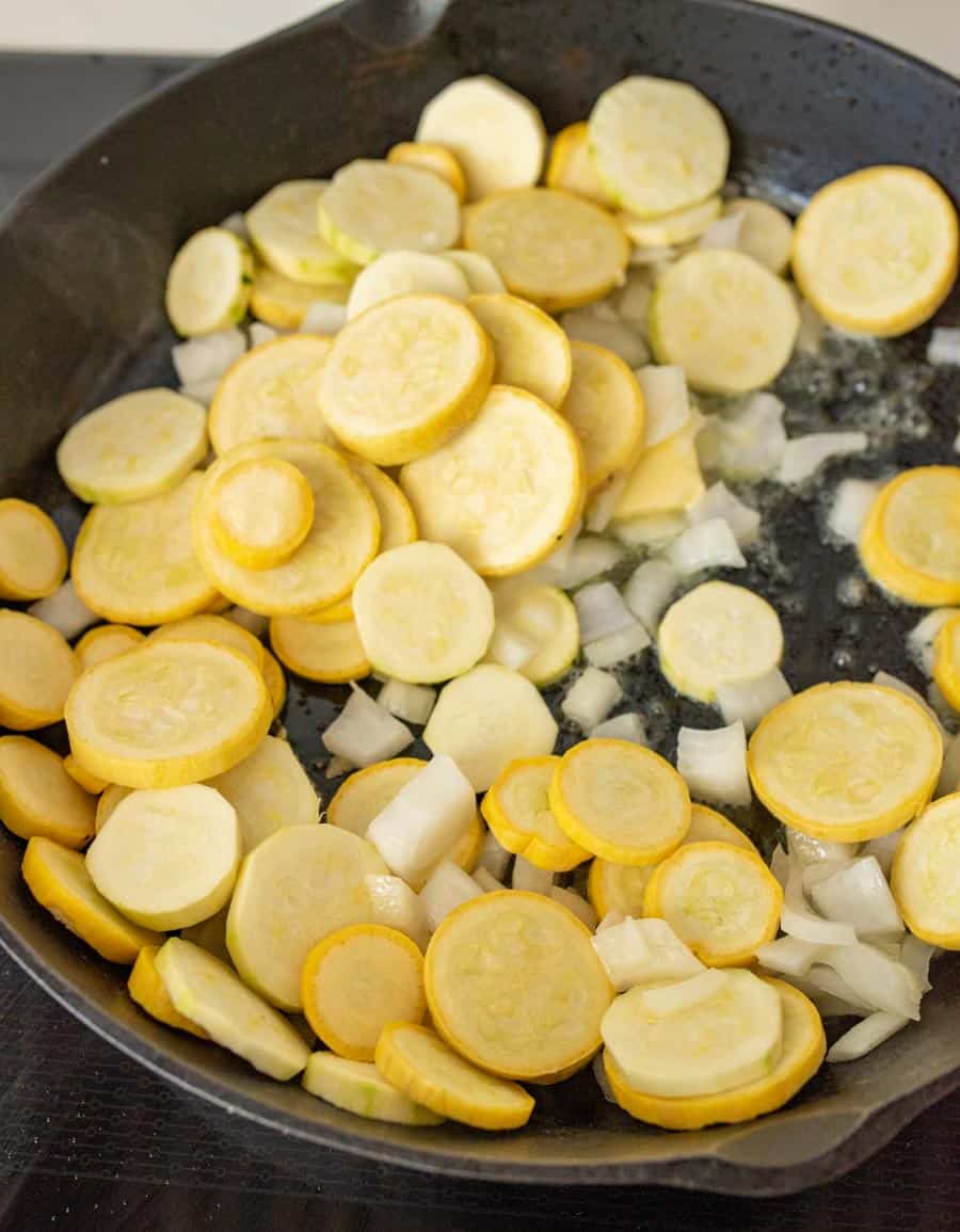 yellow summer squash and onions sautéing in a cast iron pan