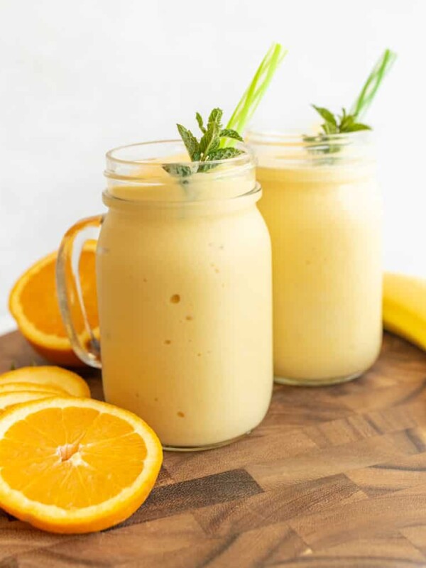 side view of two tropical yellow smoothies in mason jars with a handle