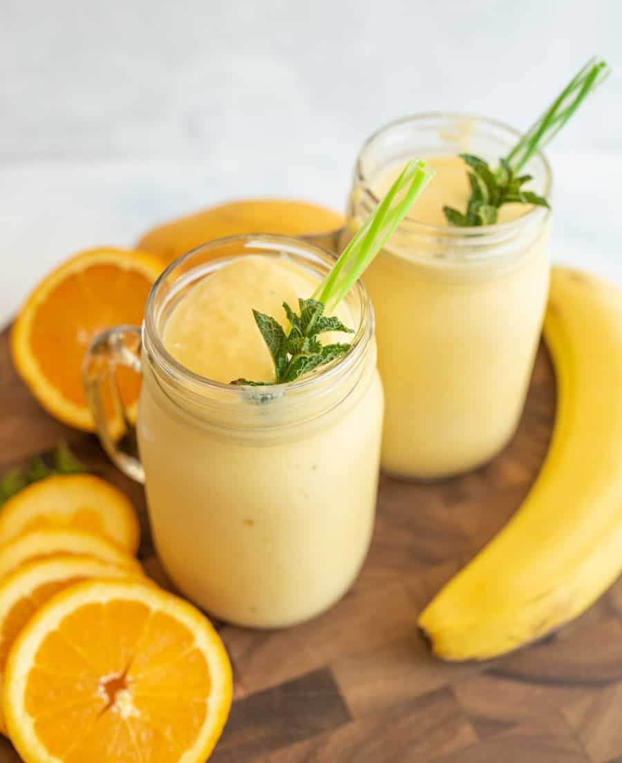 two tropical yellow smoothies in mason jars with a handle