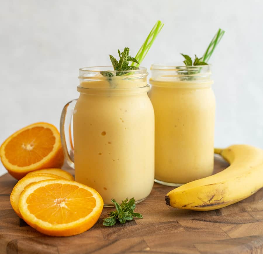 side view of two tropical yellow smoothies in mason jars with a handle