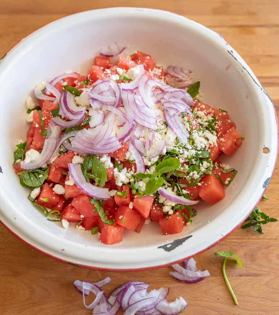 side view of watermelon and feta with the diced onions on top and the dish is not yet mixed together