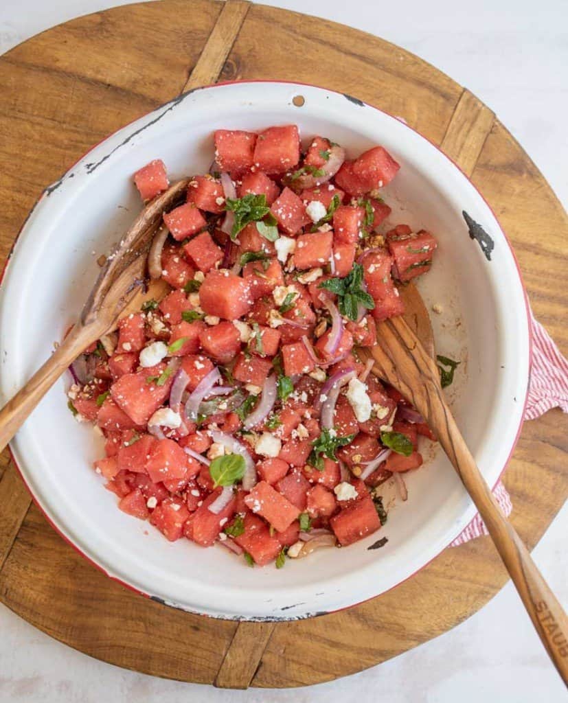 top view of watermelon and feta salad being tossed with wooden spoons