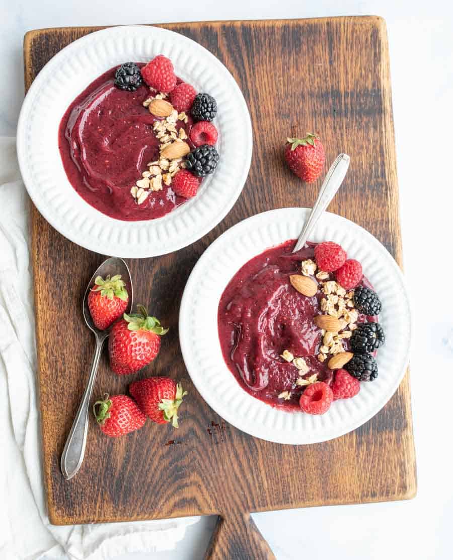 top view of two white bowls with acia bowl recipe with fresh fruit, nuts, and granola