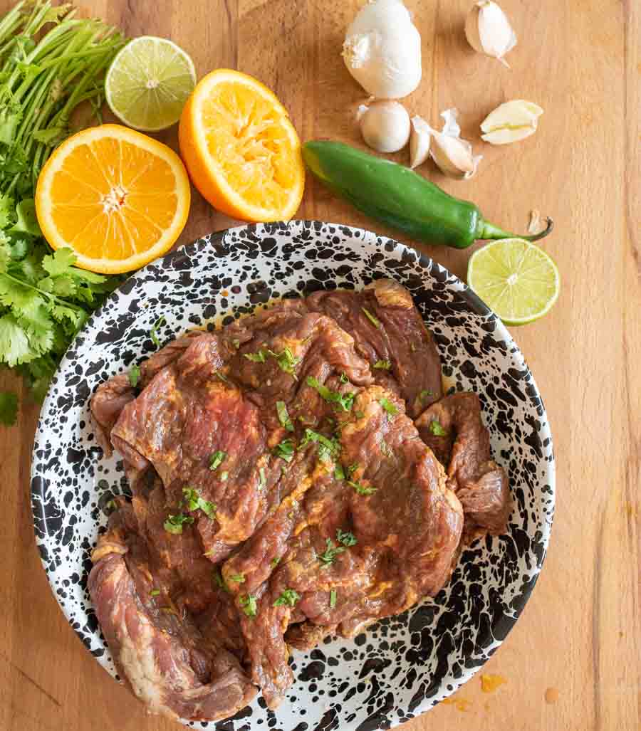 carne asada steak marinating in a black speckled bowl