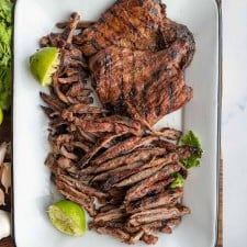 carne asada seasoned whole steak and cut steak on a white dish with limes