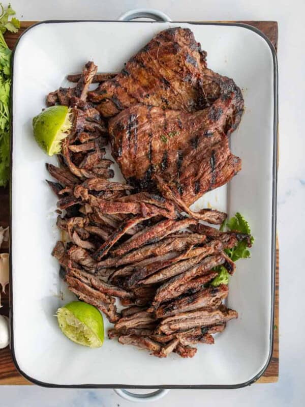 carne asada seasoned whole steak and cut steak on a white dish with limes