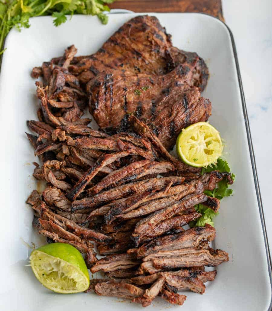 carne asada seasoned whole steak and cut steak on a white dish with limes