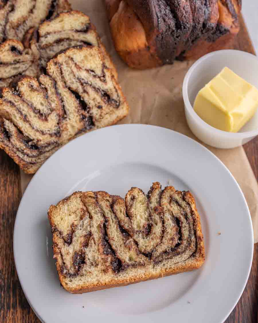 one slice of chocolate bread on a plate with the other slices and butter behind it