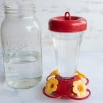 red plastic vase-like humming bird feeder next to a mason jar