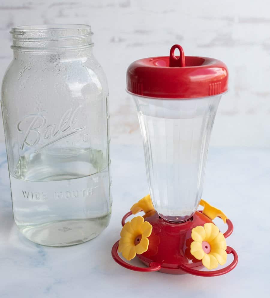 red plastic vase-like humming bird feeder next to a mason jar