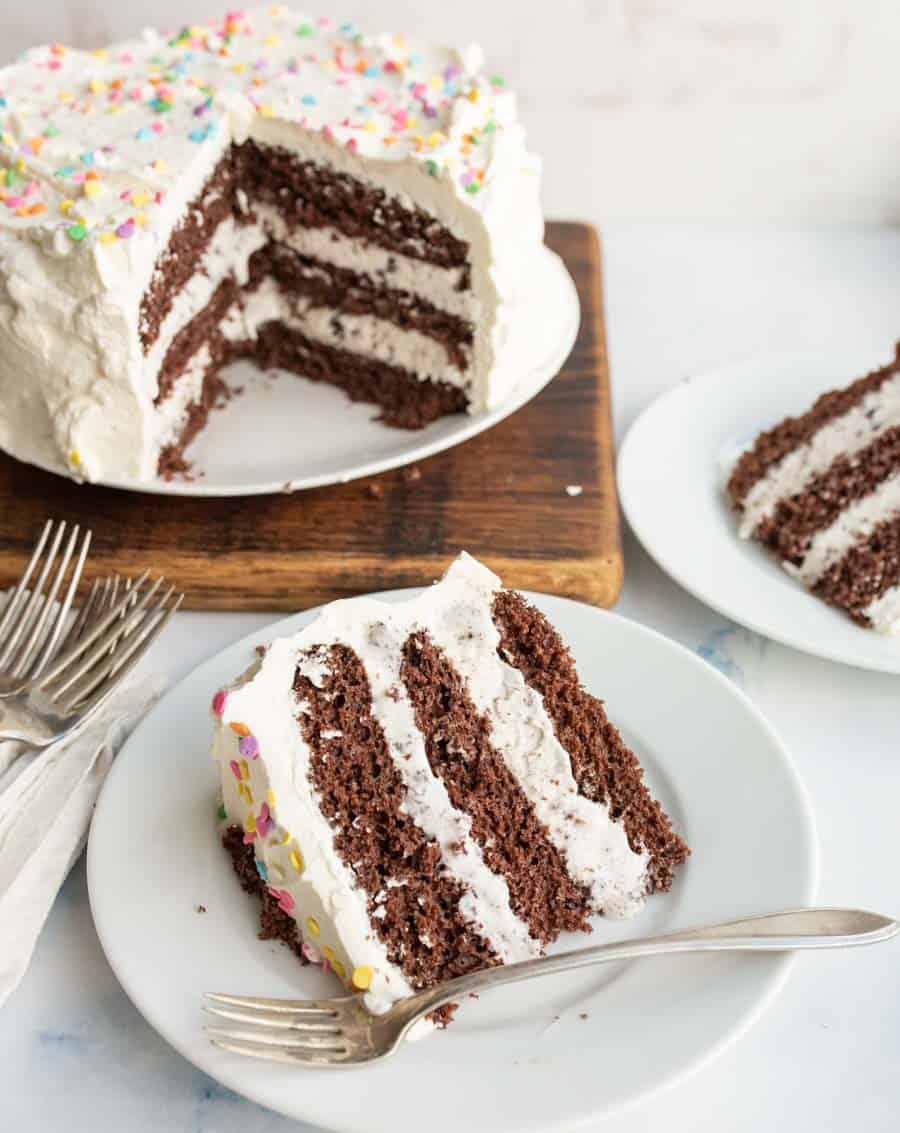 ¾ of an ice cream cake, chocolate cake and white frosting looking into the center with the slices on white plates in front