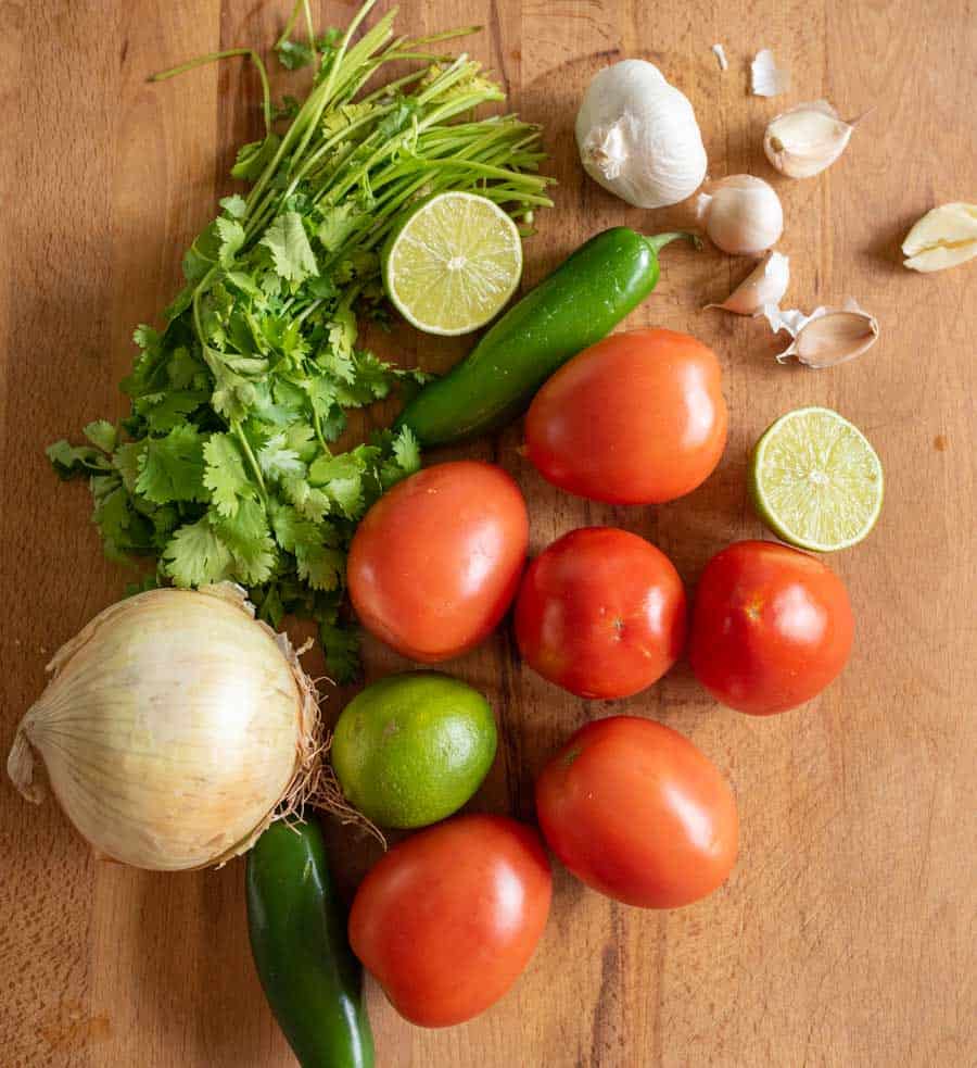 onion, tomatoes, jalapeños, garlic, lime, and cilantro on a wooden board