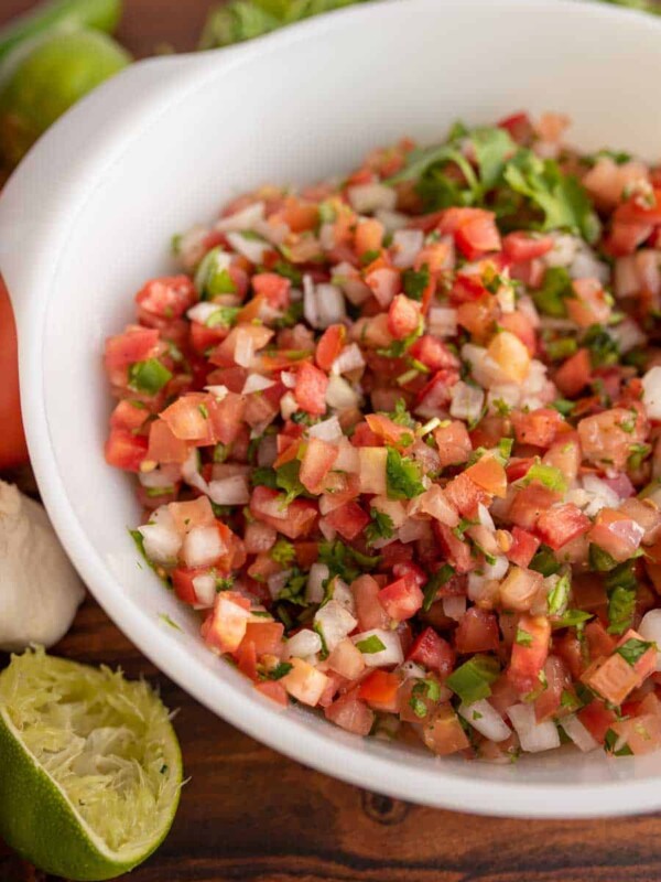 a white bowl with chunky cut tomatoes, onion, herbs in a fresh pico de gallo surrounded by limes