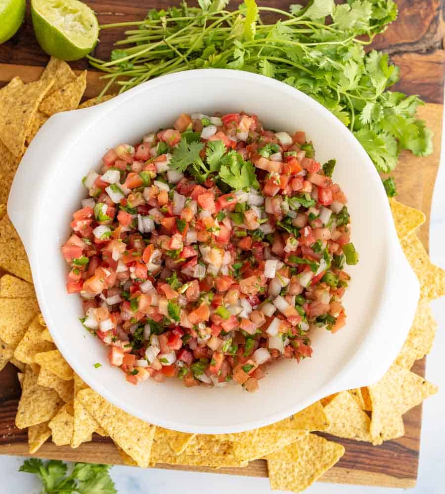 top view of a white bowl with chunky cut tomatoes, onion, herbs in a fresh pico de gallo surrounded by tortilla chips