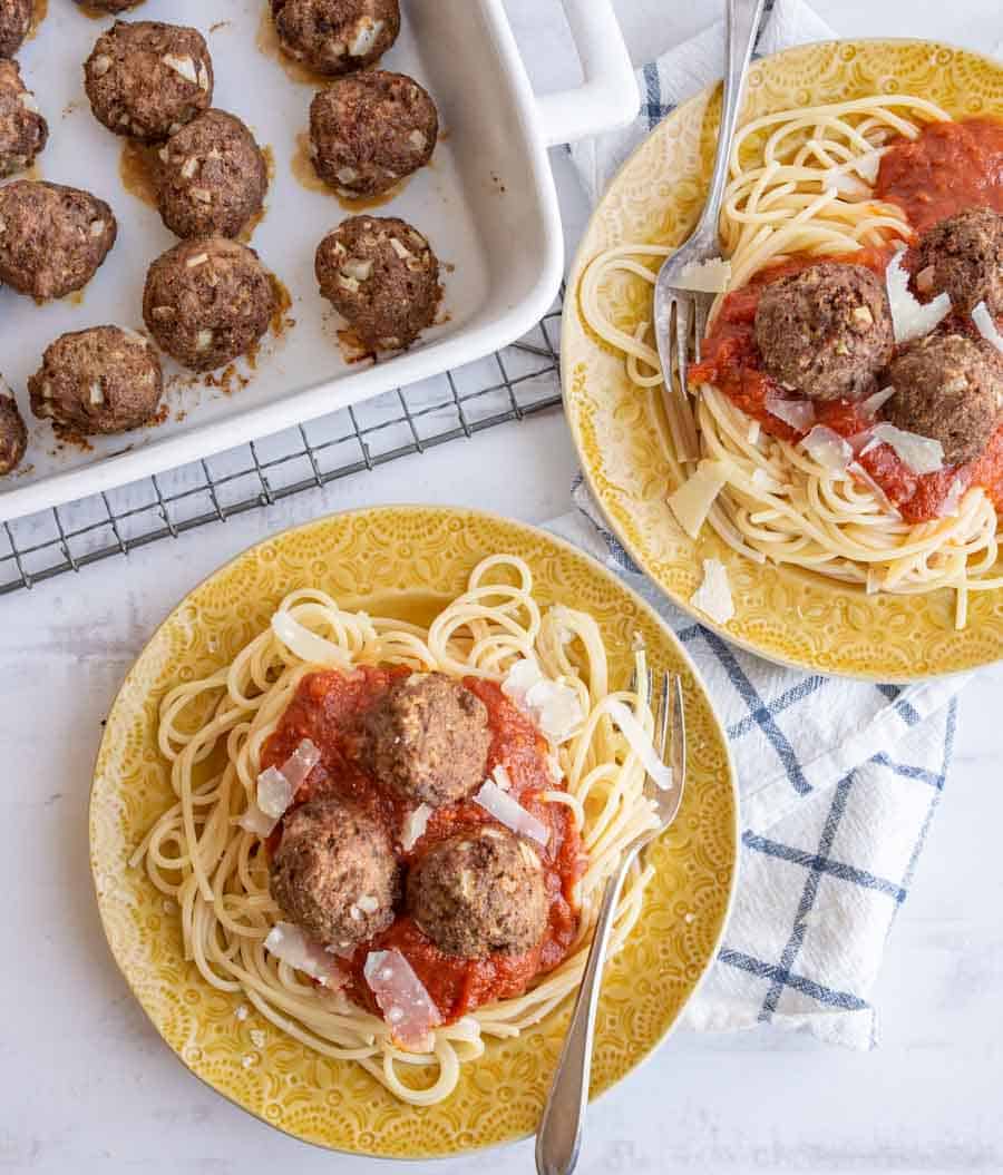 top view of yellow plate of spaghetti with turkey meatballs on top with the sheet pan of meatballs to the side