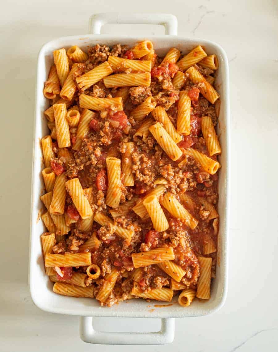 top view of a white baking dish with meaty sauce and rigatoni pasta