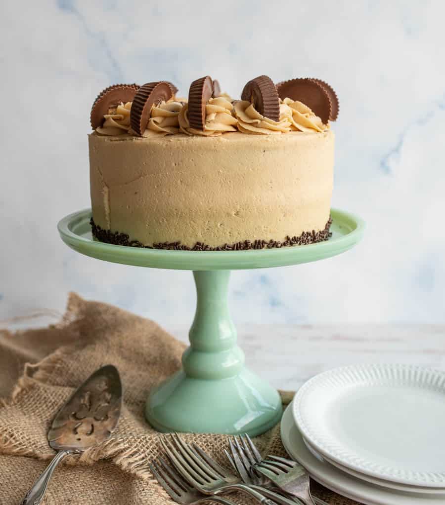 tan peanut butter frosting over a round cake with peanut butter cups on top