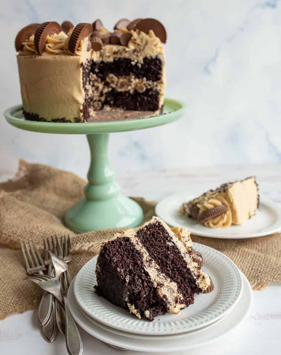 tan peanut butter frosting over a round cake with peanut butter cups on top and a slice on a white plate