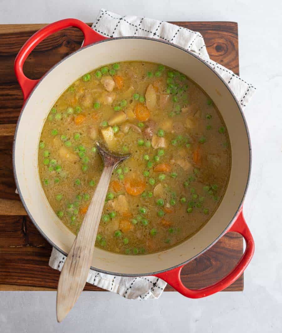 top view of green curry in a red dutch oven with a wooden spoon