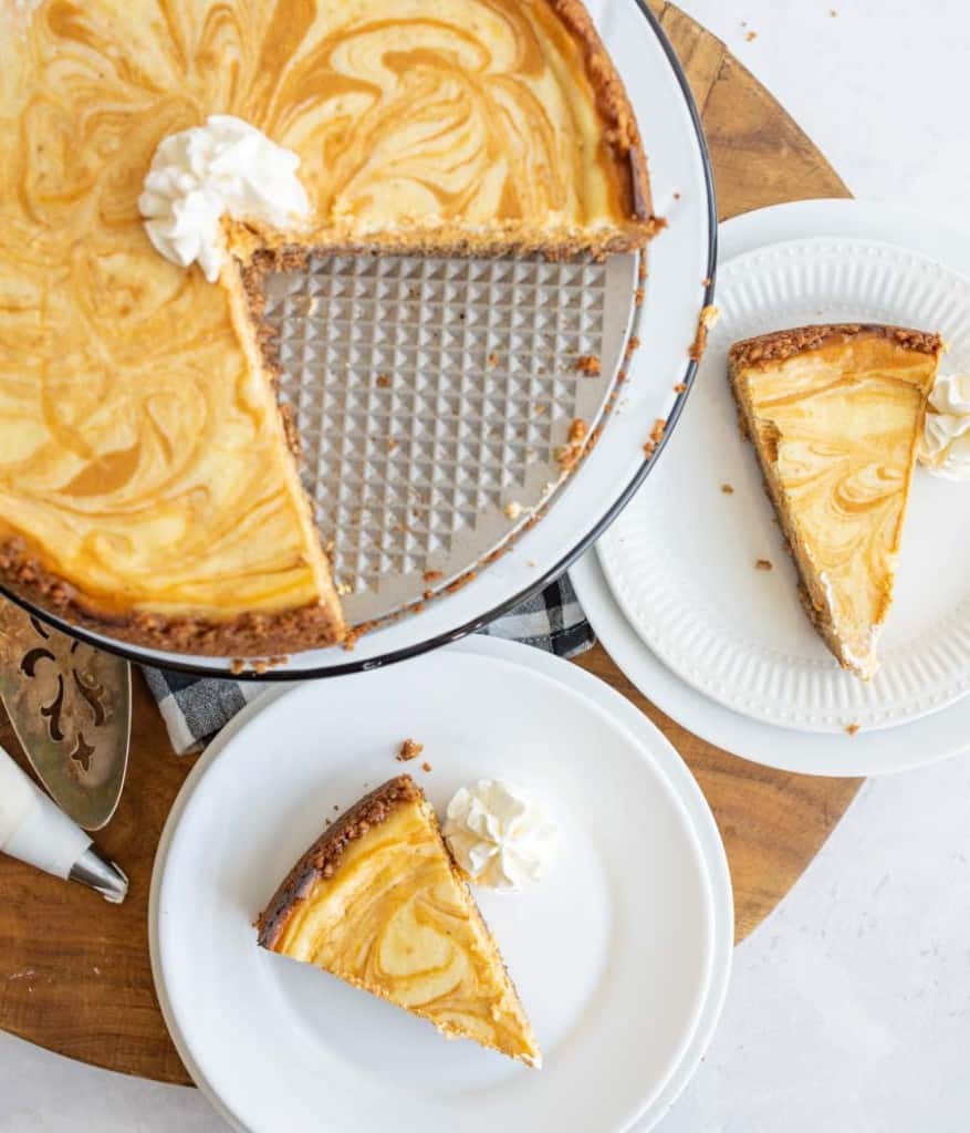 whole pumpkin cheesecake sliced and portioned onto white plates.
