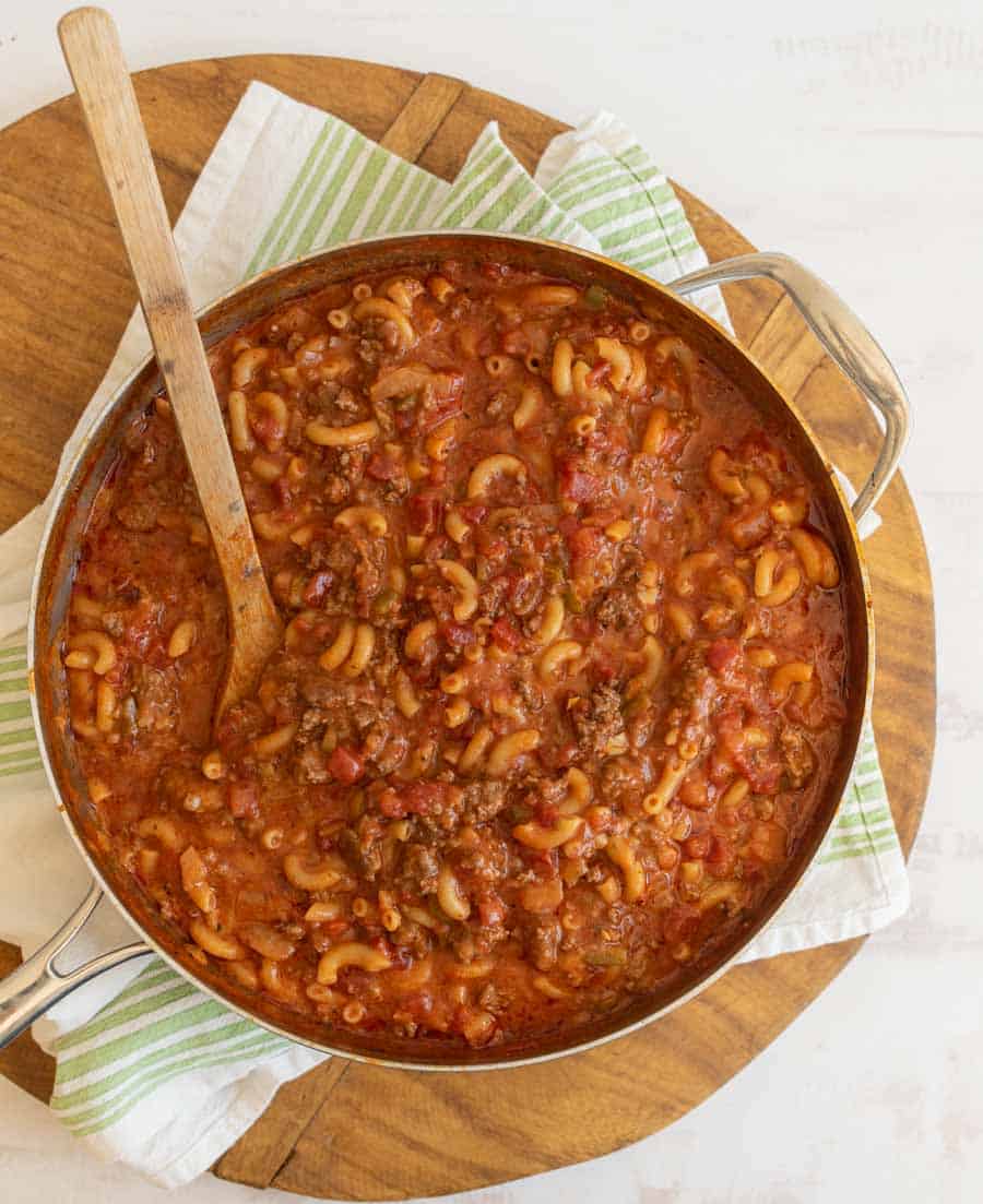 a pot of goulash which is red sauce and elbow pasta like soup with ground beef and a wooden spoon