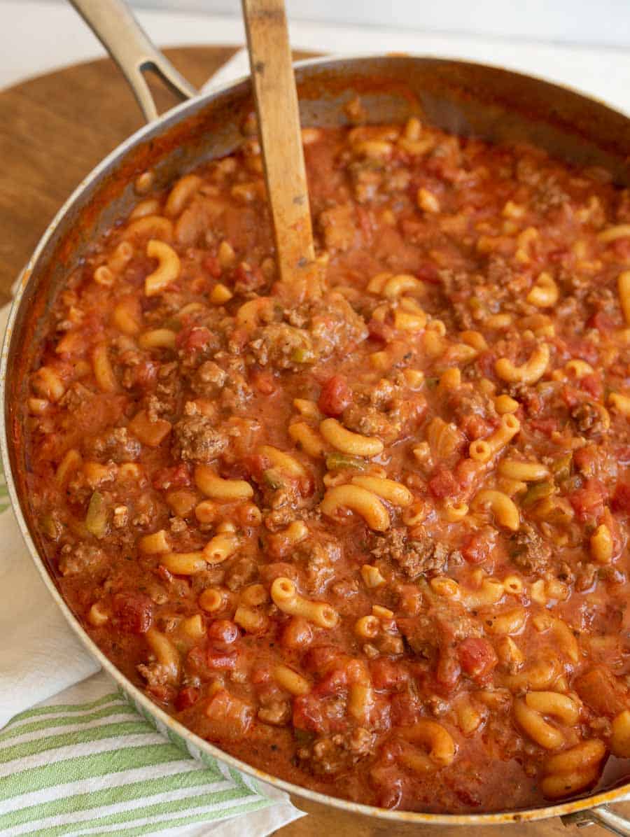 a pot of goulash which is red sauce and elbow pasta like soup with ground beef and a wooden spoon
