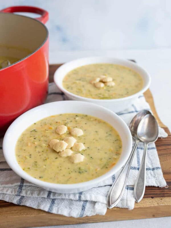 two white bowls and red dutch pot with cheddar broccoli soup and oyster crackers